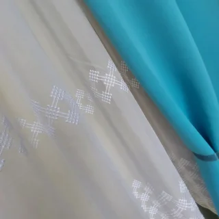 Biała firanka z wzorem w kratkę obok turkusowej zasłony